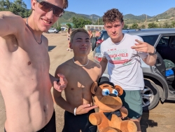 Selfie of Isaac with two other young men, all dressed for summer running and one holding a brown teddy bear wearing a hat