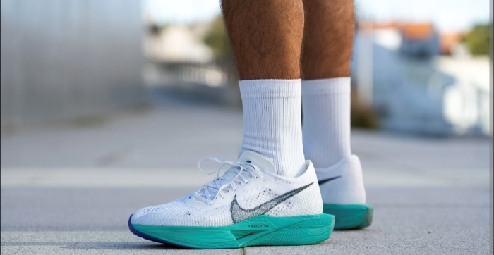 White running shoes are shown on someone wearing white socks pulled up past their calves, some hair visible on their tanned legs.