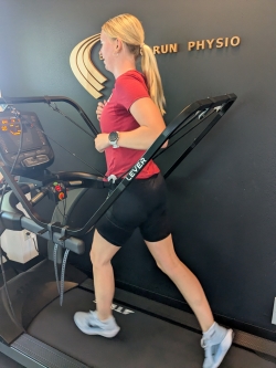 A woman runs on a treadmill, supported by a black banded bar that says Lever