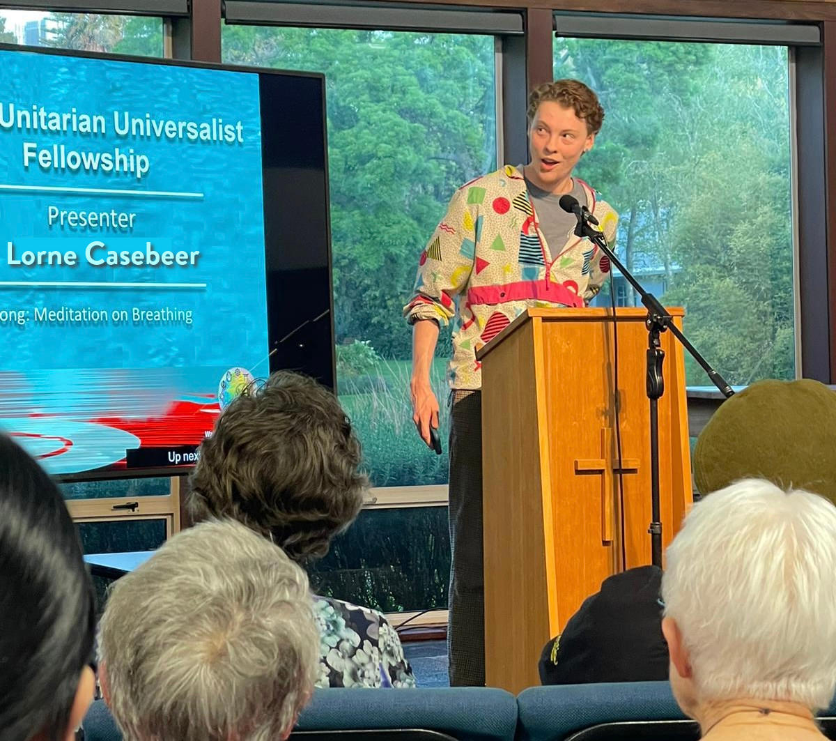 Lorne speaking in front of a crowd with a sign reading "Unitarian Universalist Fellowship, Presenter Lorne Casebeer"