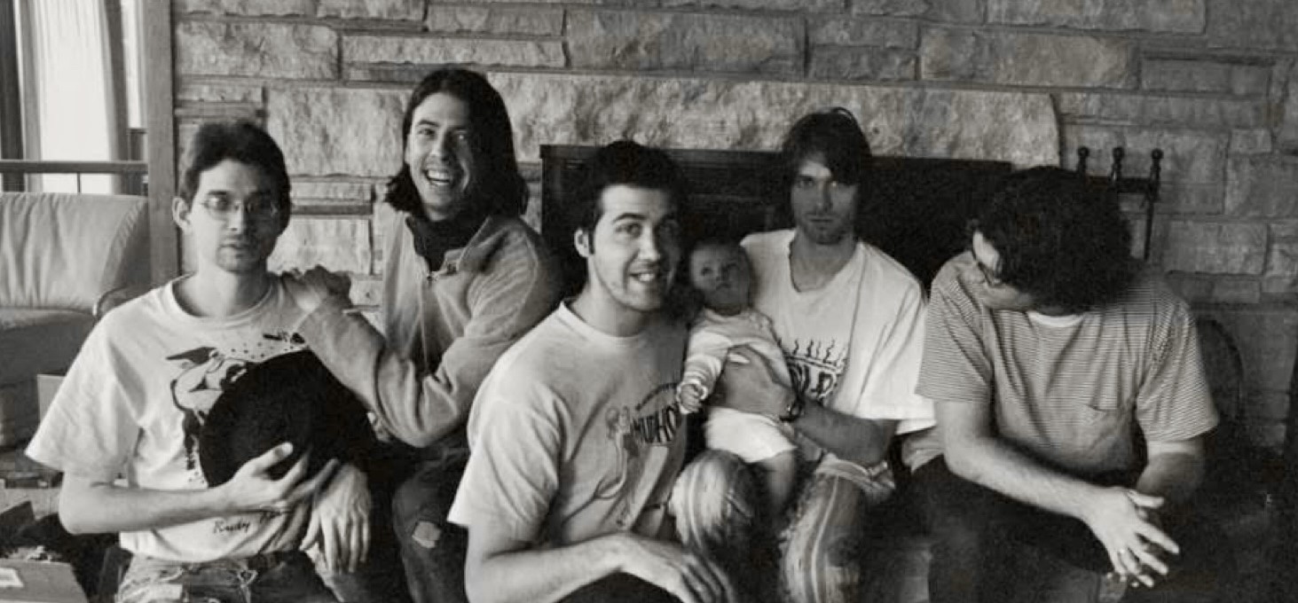 90s black and white photo of the grunge band Nirvana during their time spent at Pachyderm recording their album In Utero. One of the band members is holding the baby who appeared on the cover of this album.