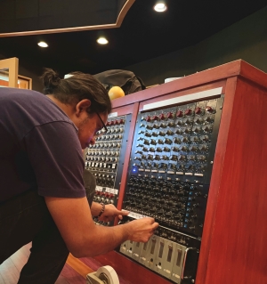 Oskar bends over to adjust settings on a complicated control board with dozens of different mechanisms for adjustment.
