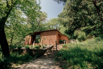 View of the modest facade of Pachyderm Studios in the Minnesota woods. It is small-looking building with wooden panels, almost like a small cabin or shack hidden in the woods.