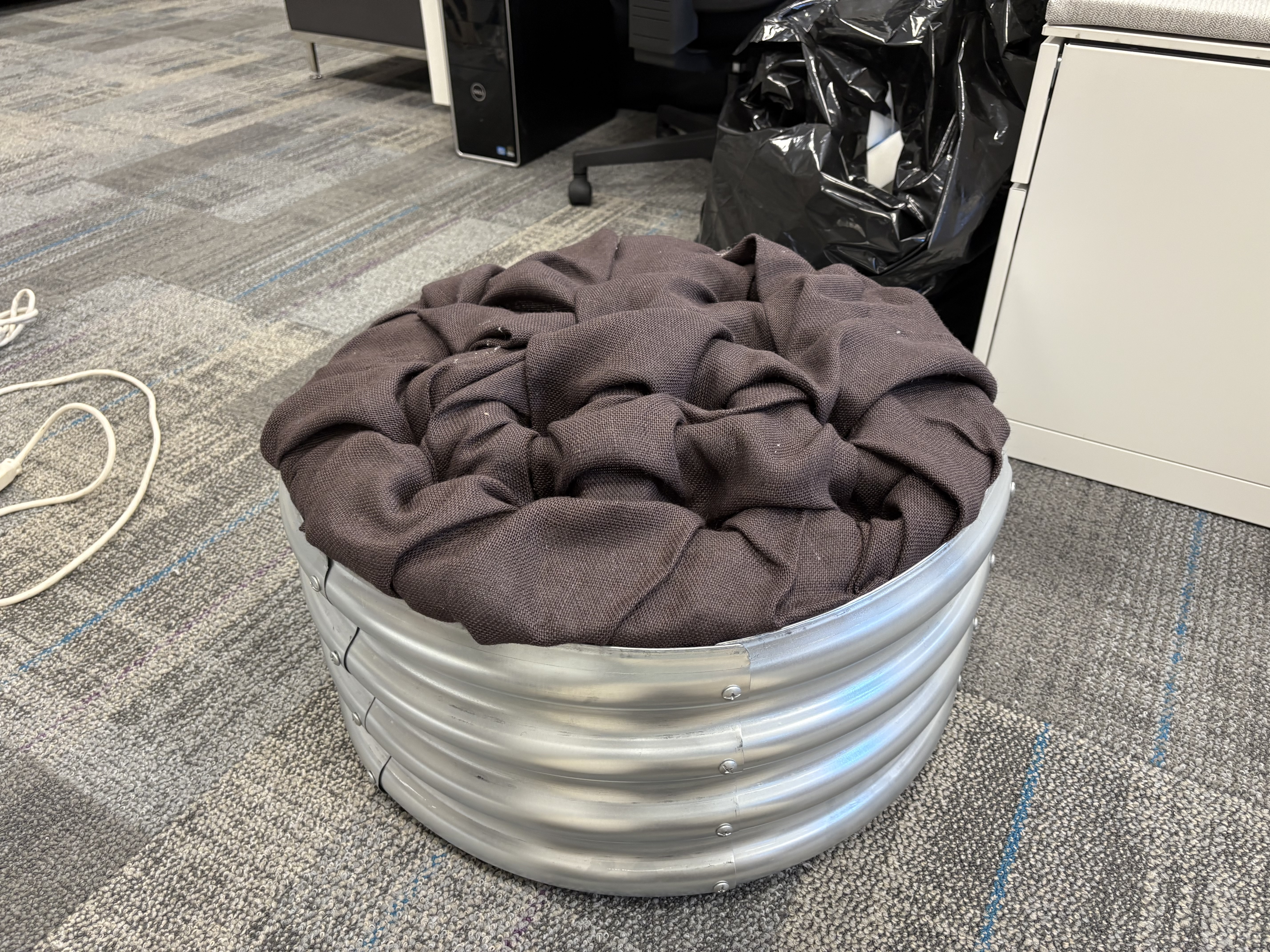 Brown fabric bundled together atop what we know is foam but looks like a wide aluminum pail