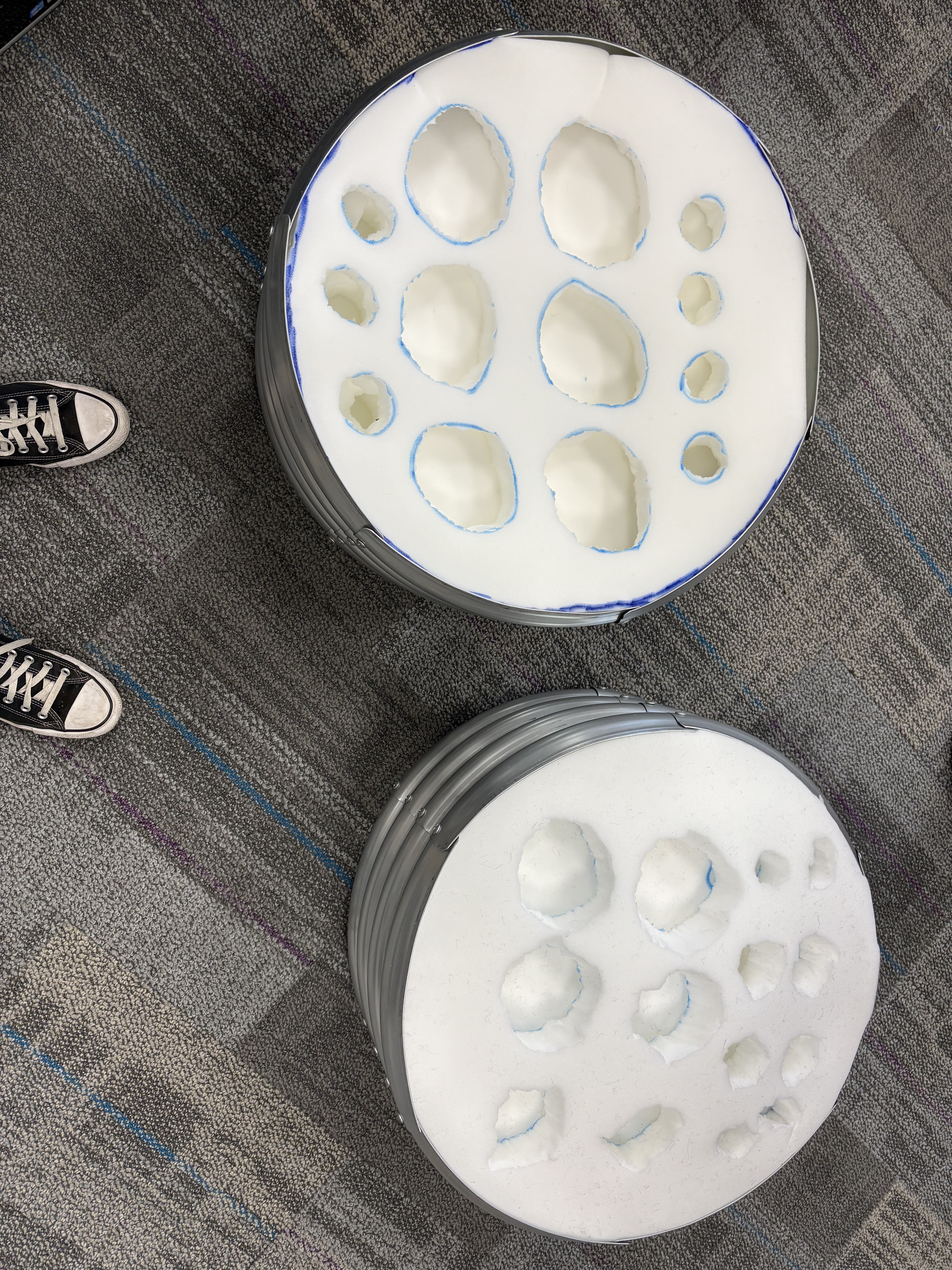The photos shows two black Converse shoes on the left and most of the frame showing stacks of foam with various sizes of oblong holes carved into them