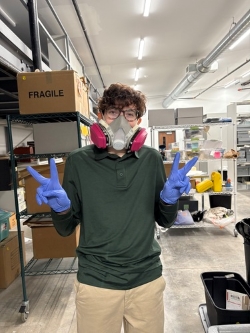 Orion flashes two peace signs from inside the AAMI archives. For protection, they are wearing a professional mask designed to filter out particulate in the air, much like a gas mask.
