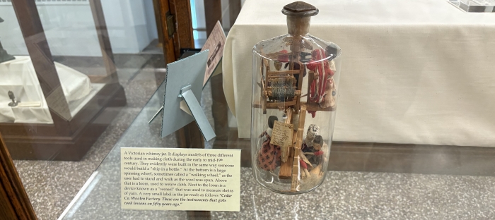 Display of a see-through glass jar with various objects inside it sitting on a see-through glass display case