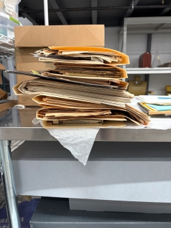 A stack of manilla folders stuffed with newspaper clippings sits on a table