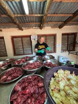 View across a table of bowls of raw meat cubes and bowls of day-old baby chicks. We can see Peyton across this table. She is wearing an Iowa Hawkeyes T-shirt and green plastic gloves as she handles the raw meat.