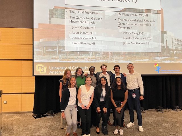 Group photo of Children's Hospital interns in front of a large projector screen, likely on the stage of an auditorium