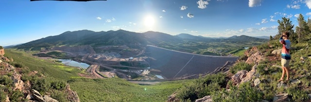 Sprawling view of a mountain valley area with Sean to the far right holding his left hand up as a visor to shield his face as he takes in the view