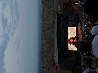 View of a movie screen from far up in stadium seating of an outdoor ampitheatre. The screen shows Pirates of the Caribbean as we can see the character Captain Jack Sparrow.