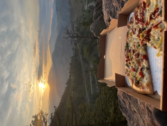 Looking out at a sunset over a pizza with multiple toppings and one slice already eaten