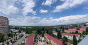 View from several stories up looking out at brick adjacent brick buildings and a beautiful blue sky with some fluffy white clouds