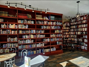 Image shows a bookshelf taking up an entire wall with a little nook corner created by a neighboring bookshelf. The bookshelves are a wooden mahogany color with multiple colors of books shelved vertically with their spines facing out.