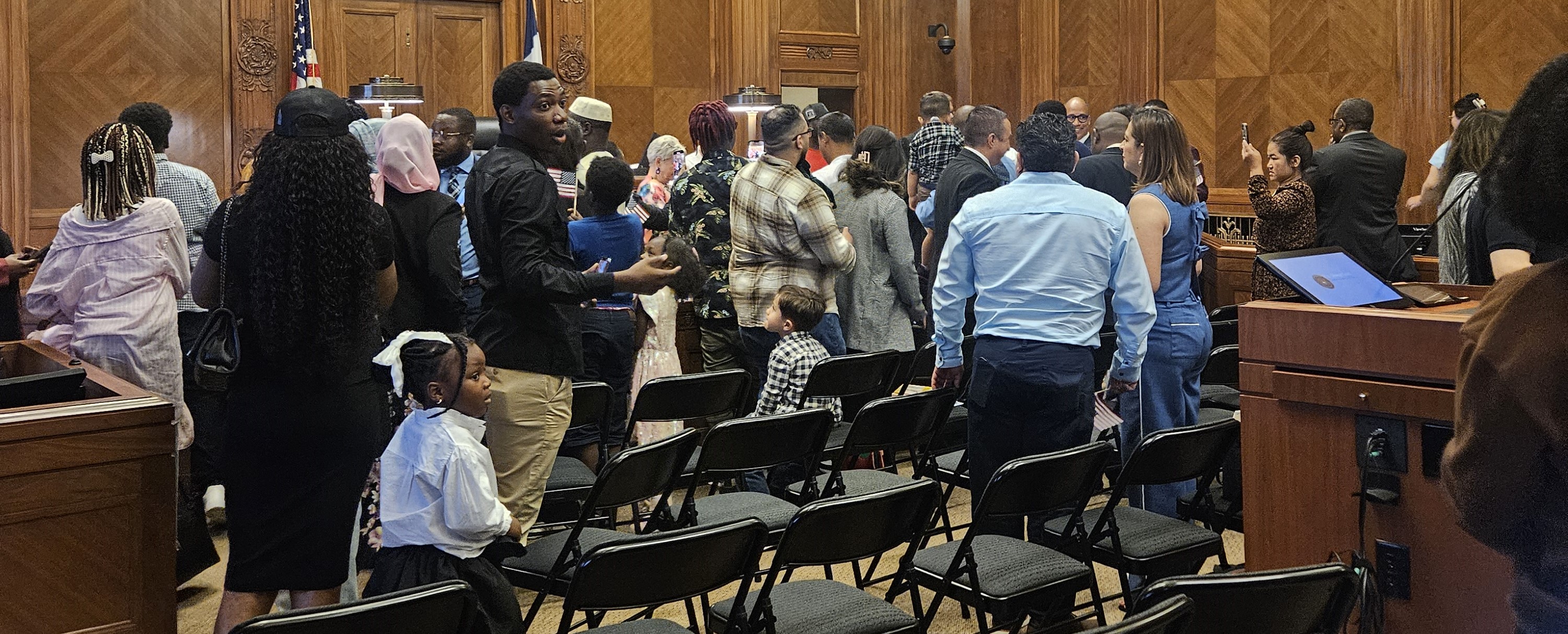 A diverse crowd of individuals standing around a courtroom, most dressed business casual to formal