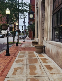 Pedestrian view of a sidewalk in Davenport with brick-lined buildings and an old, black clock fixture hanging suspended over the street ahead