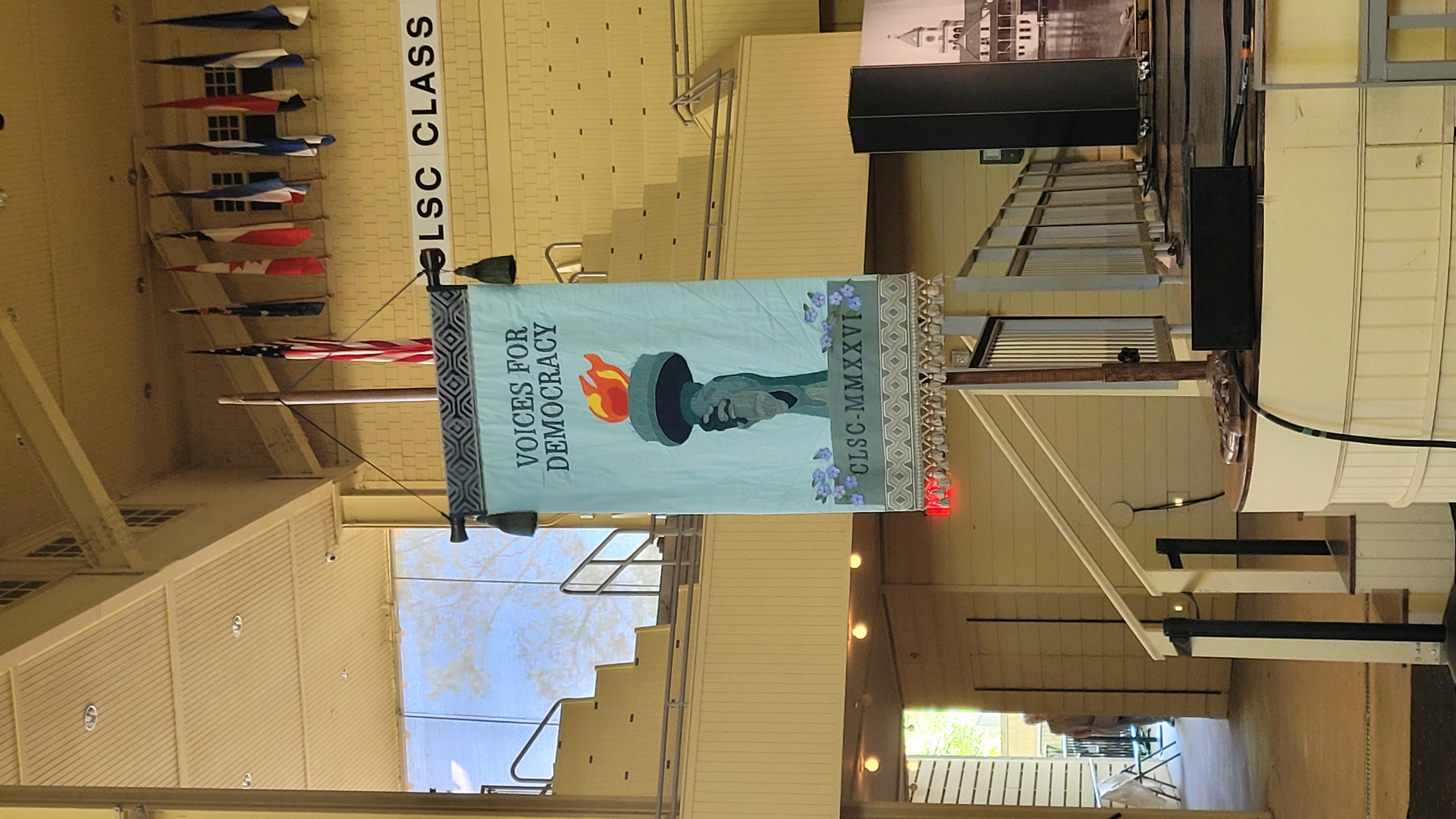 Sign saying Voices for Democracy in a large wood-paneled room with a staircase.