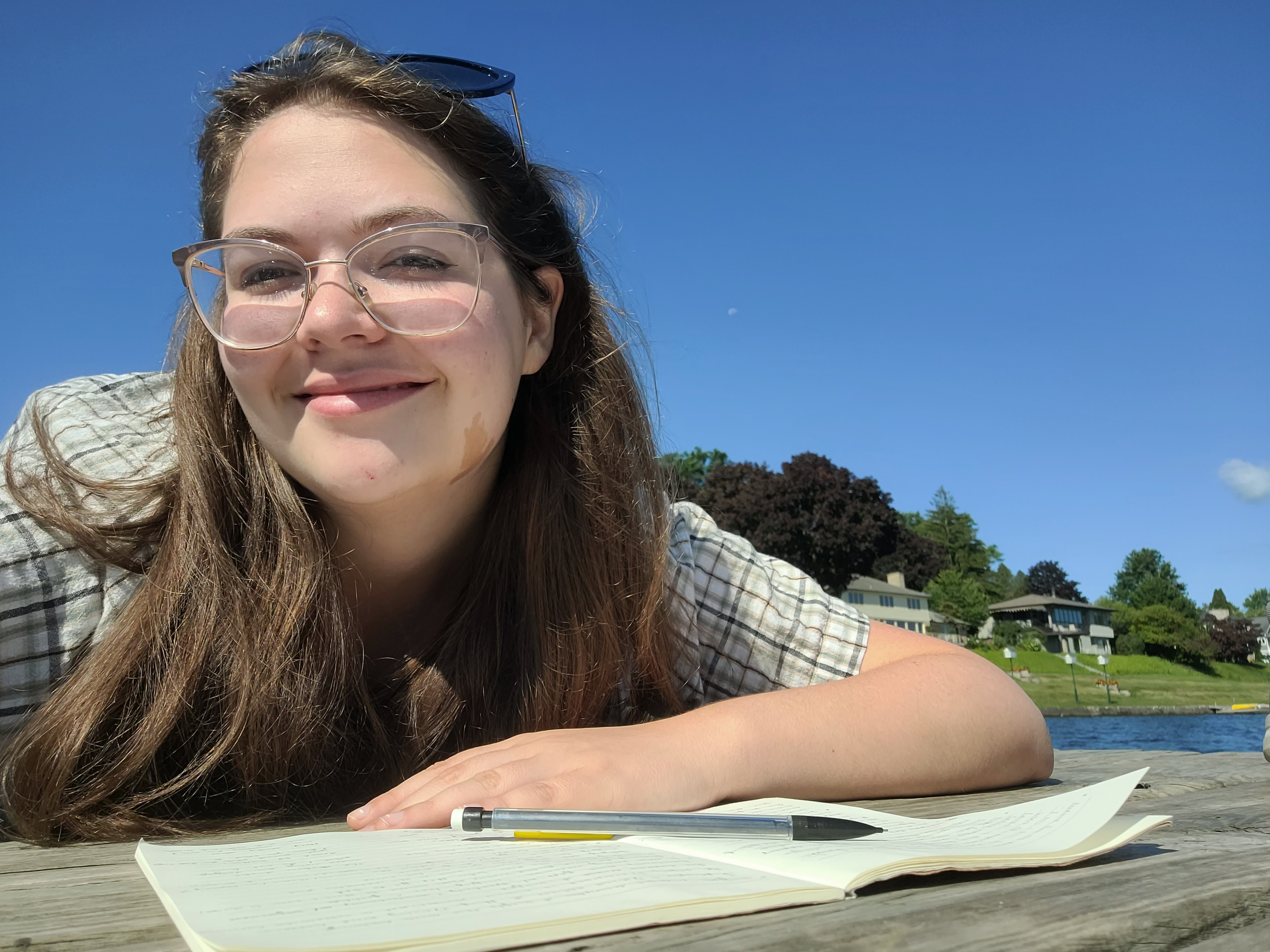 Young woman writing in a notebook on a dock by a lake.