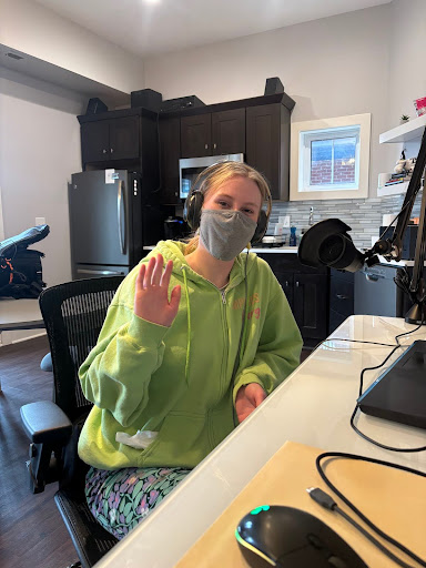 Chrysalis sitting at a desk waving to the camera wearing a mask