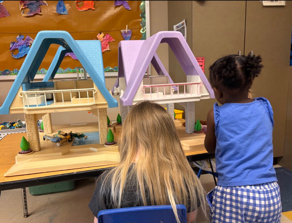 Two preschool-aged children play in a dollhouse.