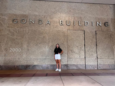 Payton stands against a marble-looking wall with gold-plated letters a few feet above her reading "Gonda Building" and, several feet to the left of her in the photo, the year 2000 can be seen.