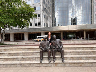 Two bronze statues sit on a set of steps outside a building, and Payton poses behind and in between the statues.
